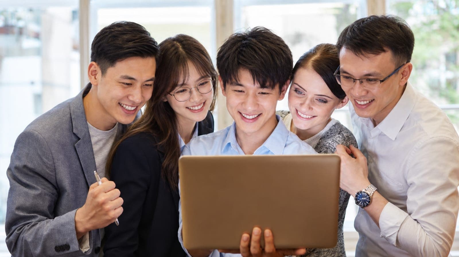 Five teammates crowded around a laptop, smiling